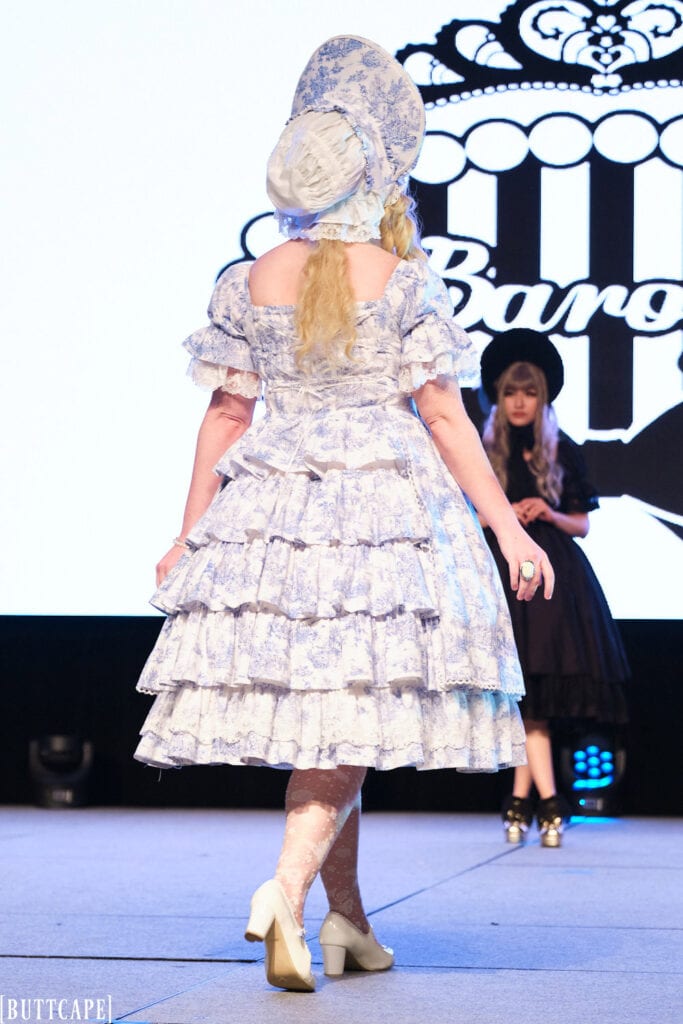 lolita model wearing white dress with blue print plus matching bonnet walking away.