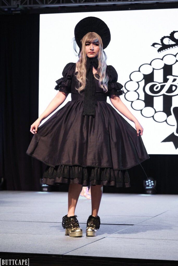 lolita model wearign all black dress and bonnet holding sides of dress outwards.
