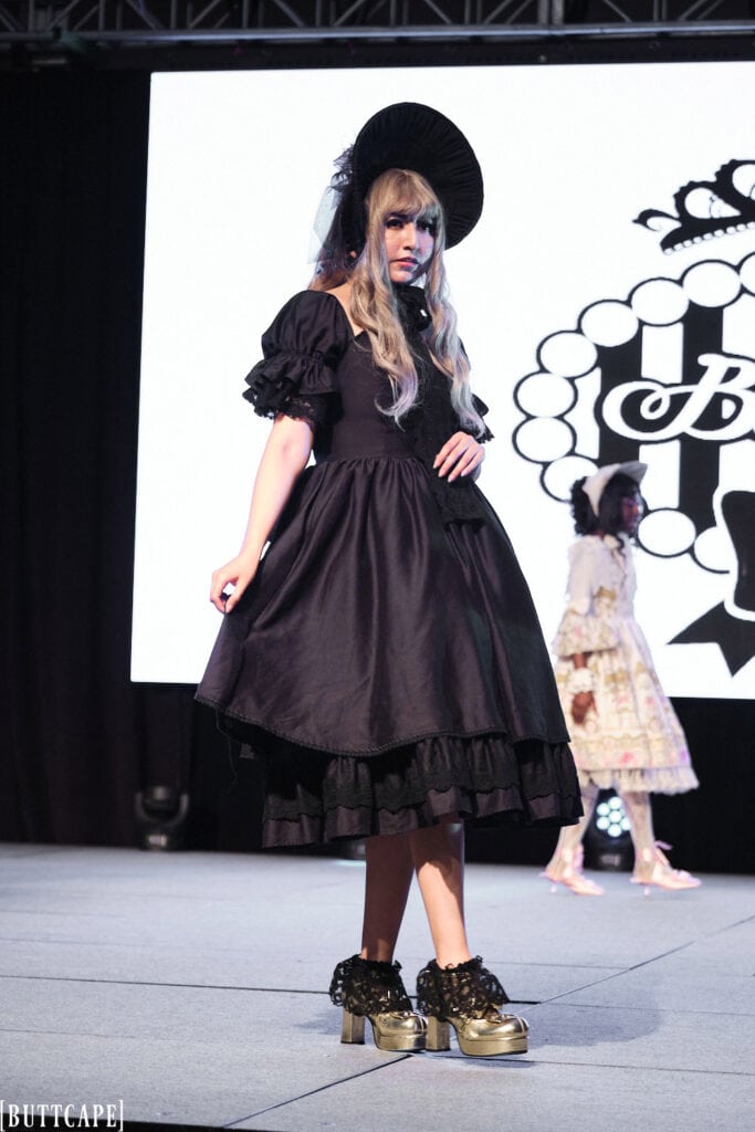 lolita model wearign all black dress and bonnet posing three quarters view.
