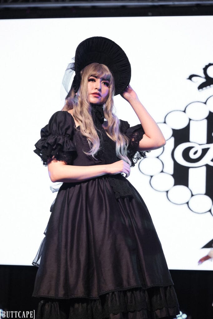 lolita model wearign all black dress and bonnet portrait with hand on bonnet.