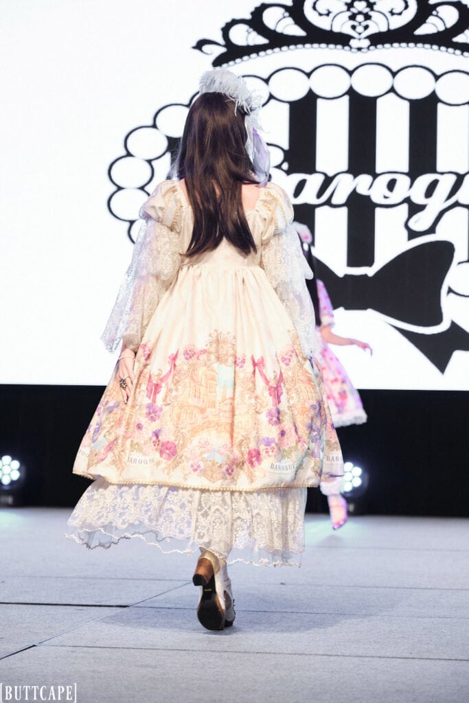 lolita model wearing white and gold print dress with lace accents walking away.