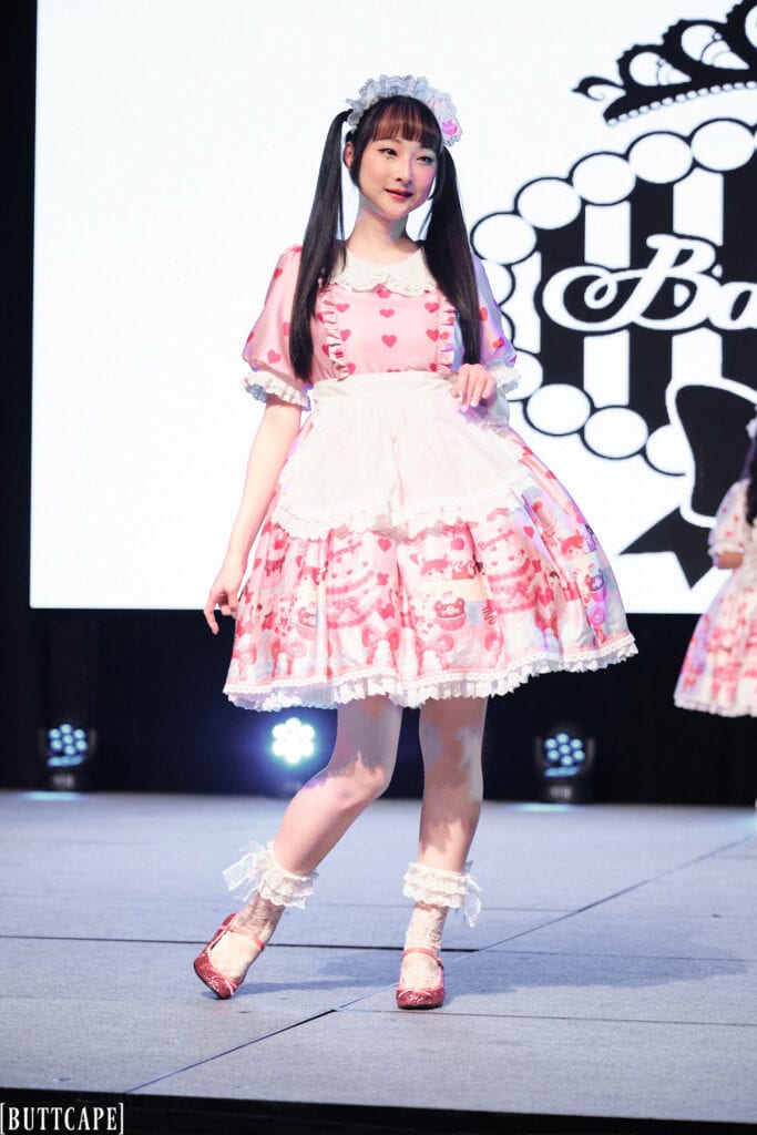 lolita model Rin Rin Doll wearing pink dessert print apron dress posing.