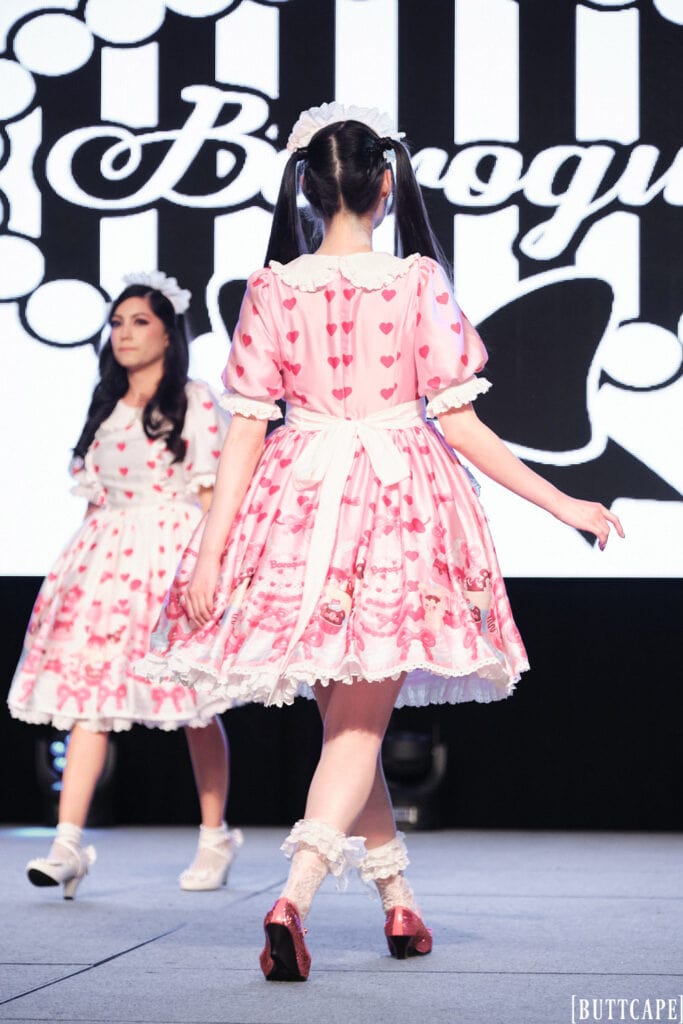 lolita model Rin Rin Doll wearing pink dessert print apron dress exiting stage.