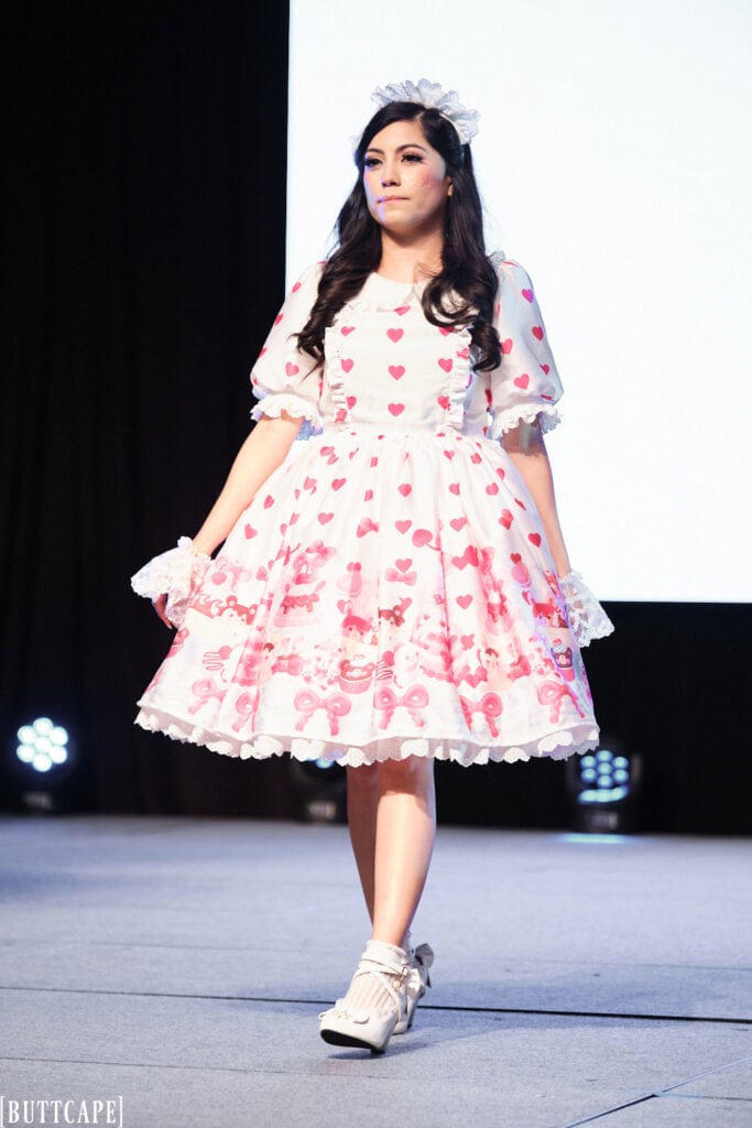 lolita model wearing white and pink dessert print dress walking towards front of stage.