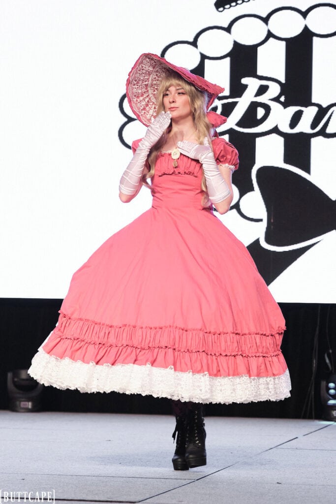 lolita model wearing extravagant pink gown and hat walking towards audience.