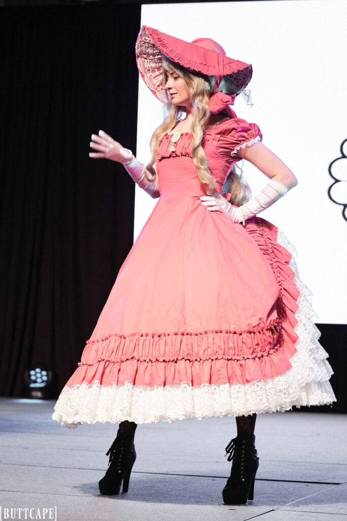 lolita model wearing extravagant pink gown and hat posing towards side.