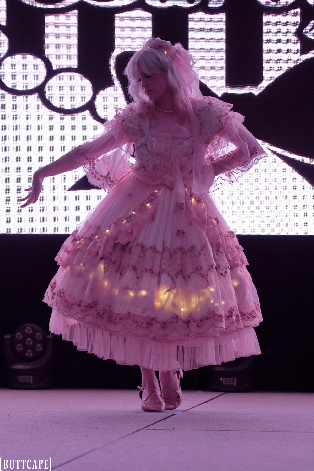 lolita model wearing lacy pink dress with LED lights in dark posing.