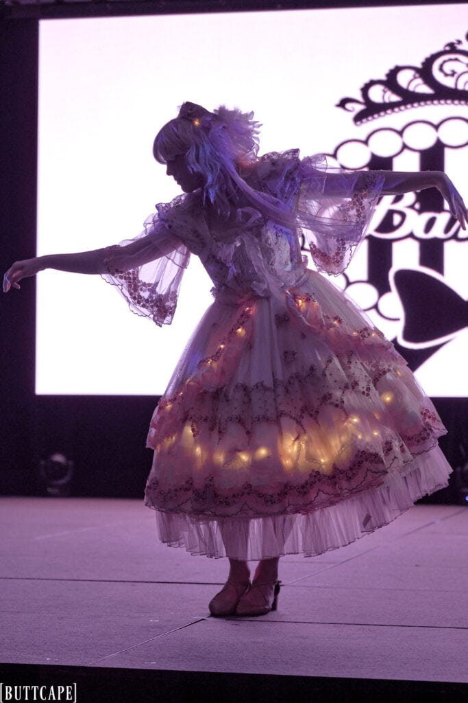 lolita model wearing lacy pink dress with LED lights in dark bowing.