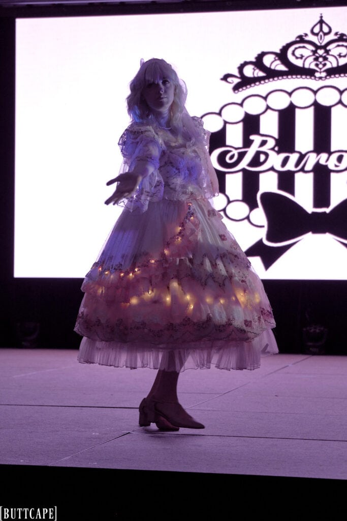 lolita model wearing lacy pink dress with LED lights in dark with hand extended.