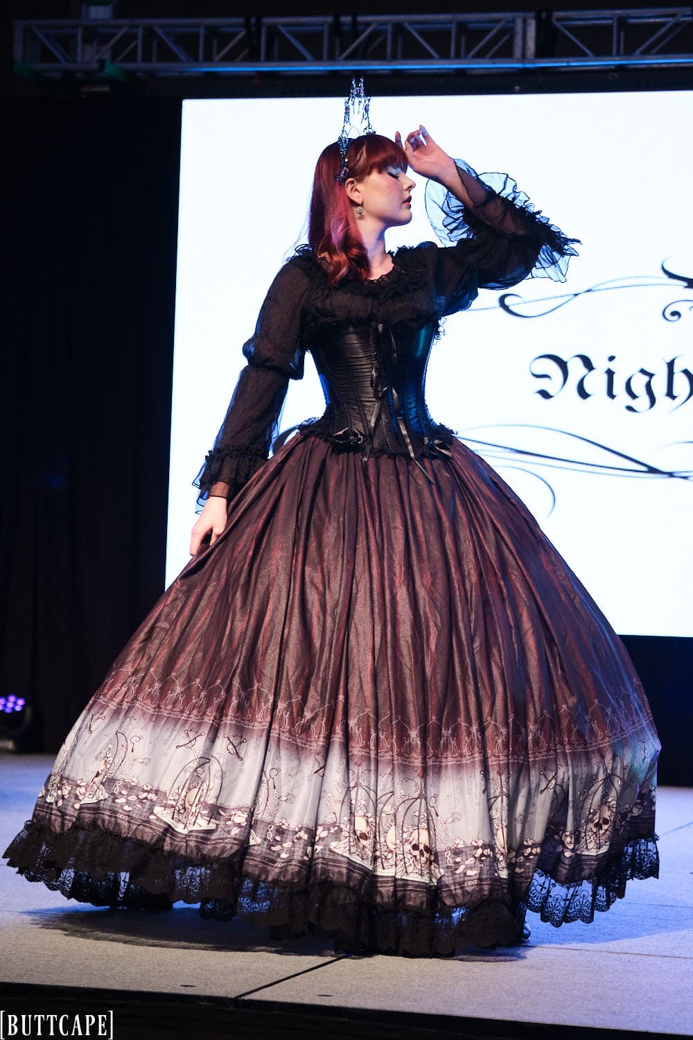 gothic model wearing floor length gown posing with arm up.