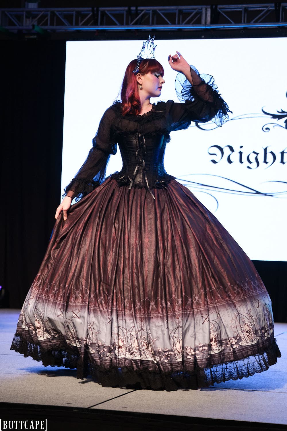 gothic model wearing floor length gown posing with arm up and holding skirt out.