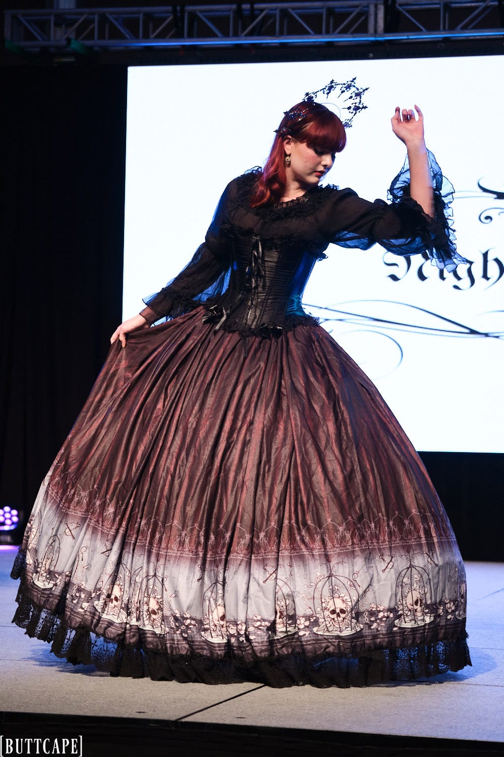 gothic model wearing floor length gown posing with arm up and looking down.