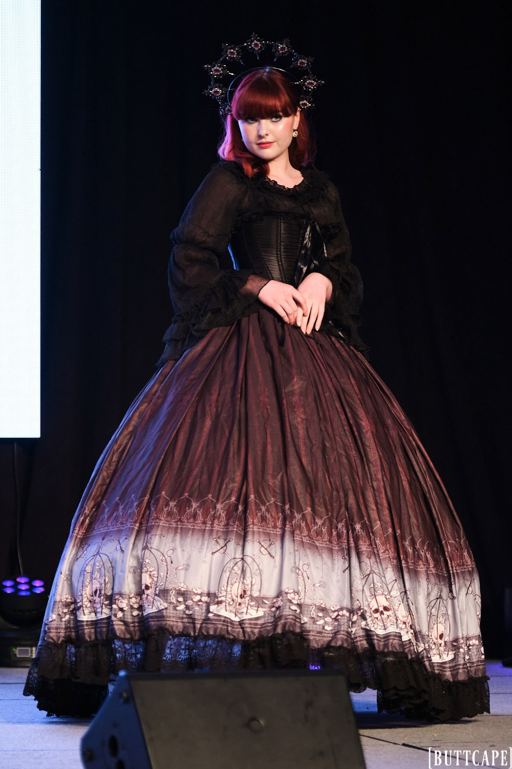 gothic model wearing floor length gown posing with hands in front of waist.