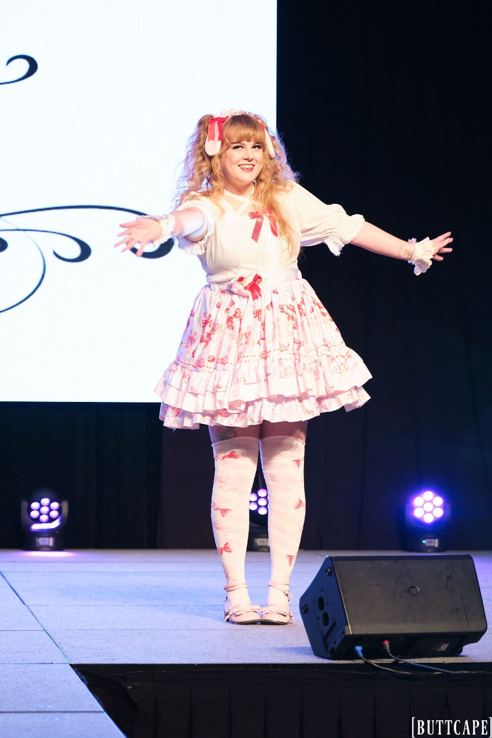 sweet lolita model wearing white blouse and pink skirt posing at end of runway.