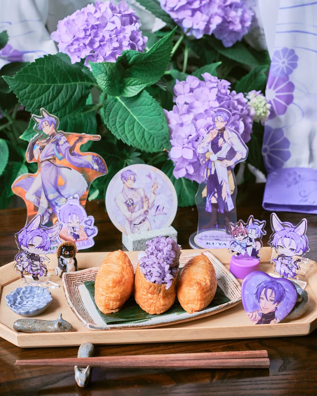 tray of inarizushi decorated with anime merchandise and hydrangea in background.