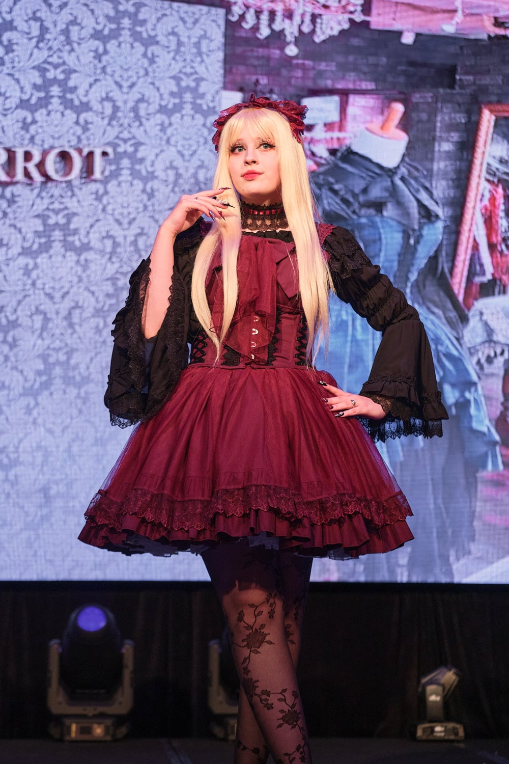 Model wearing red tulle lolita dress, corset, black blouse, lace headdress, and lace tights - half body 2.