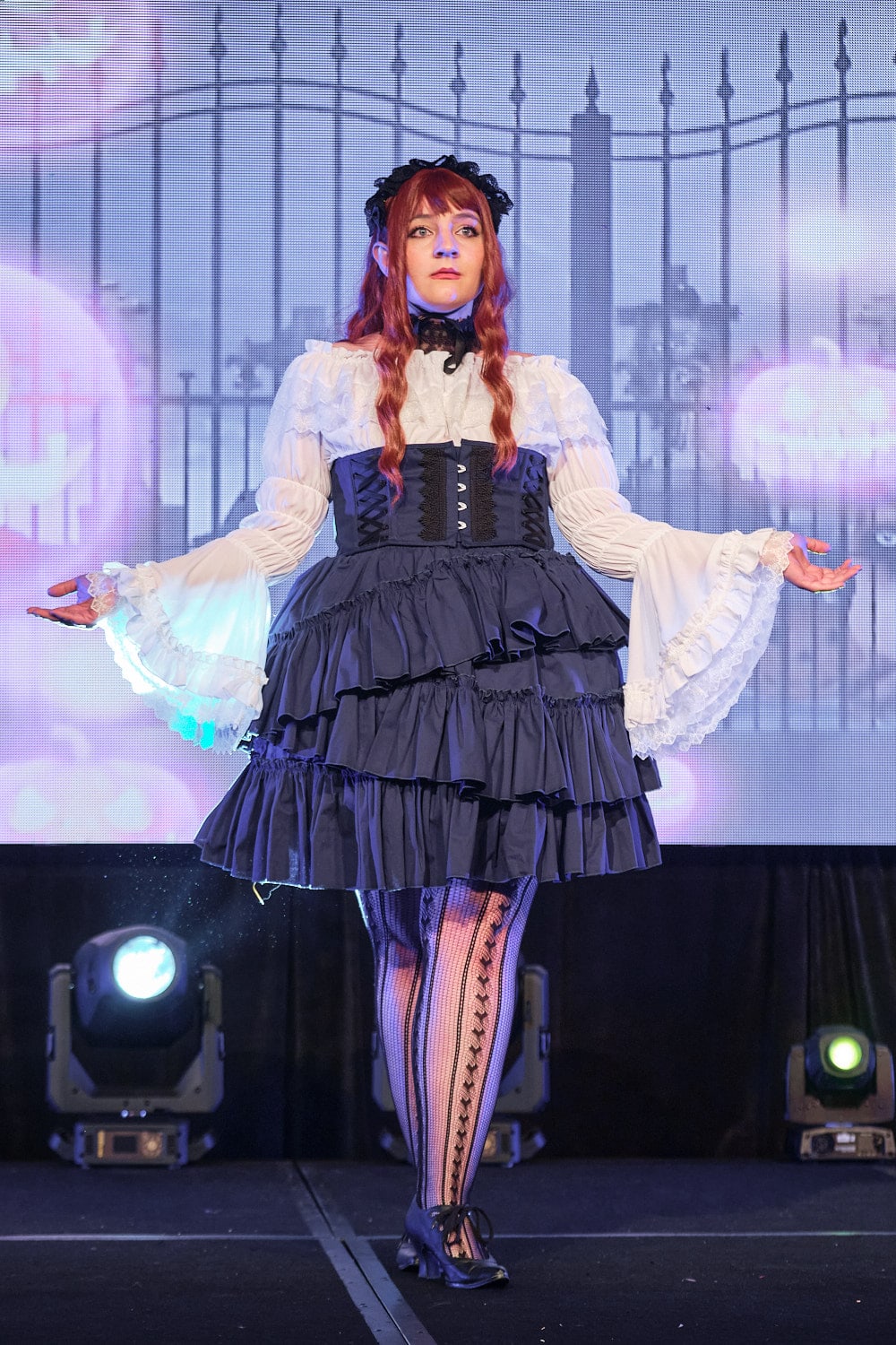 Lolita fashion model wearing lace headdress, white frilly blouse, navy corset, and navy tiered skirt - full body 2.