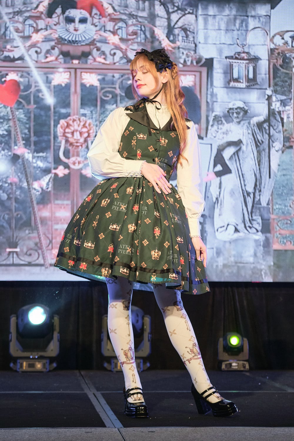 Classic lolita wearing green vest JSK with crown and key allover print, white blouse, and white matching print tights - fullbody.