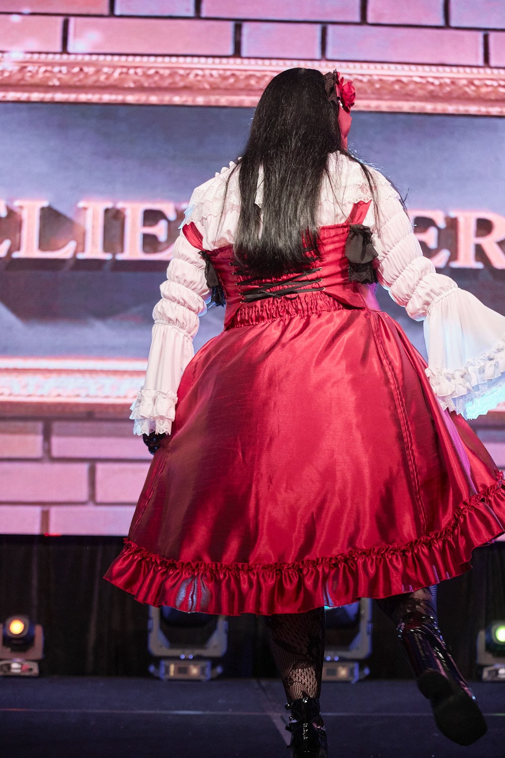 Plus size gothic lolita wearing red and black shantung bustle dress with white princess sleeve blouse, lace tights, and black shoes - backside.