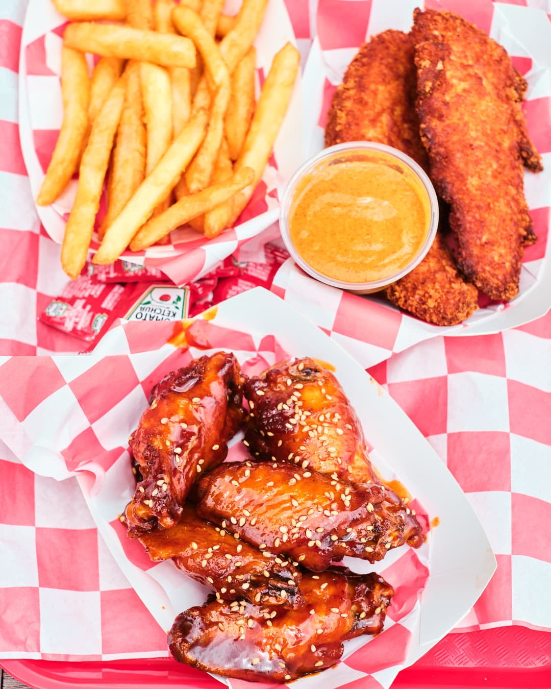 overhead shot of tray with french fries, chicken tenders with dipping sauce, and saucy wings.