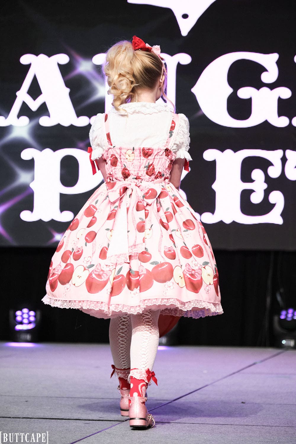 Model 3 wearing pink and red cherry themed lolita outfit holding red heart purse - back view.