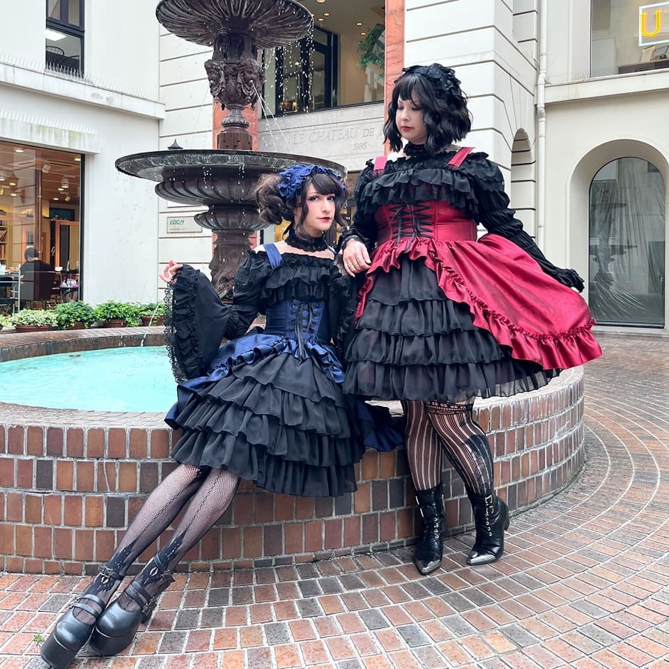 Two gothic lolitas sitting on fountain.