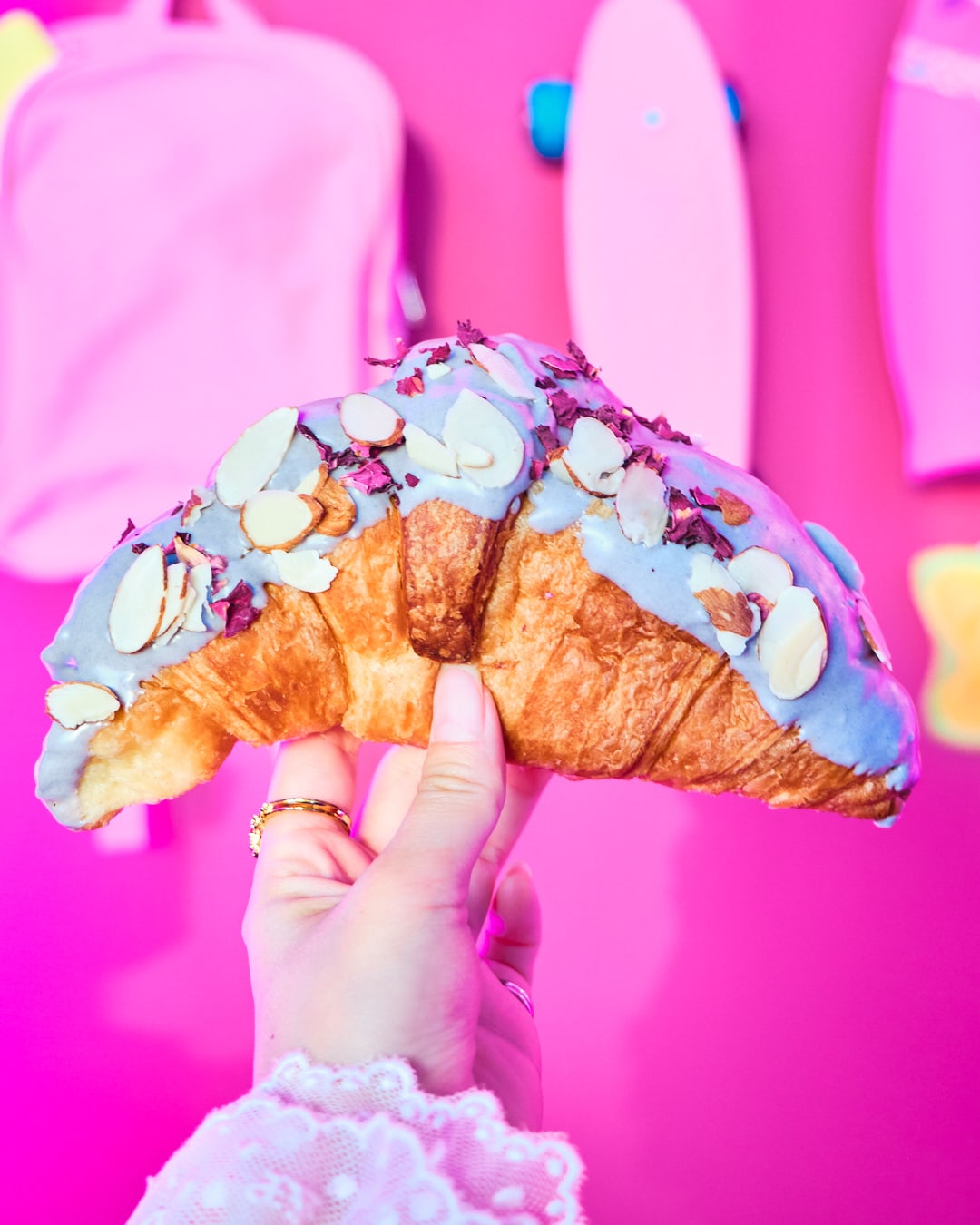 Croissant half dipped in purple ube chocolate sprinkled with almonds and rose petals being held in hand.