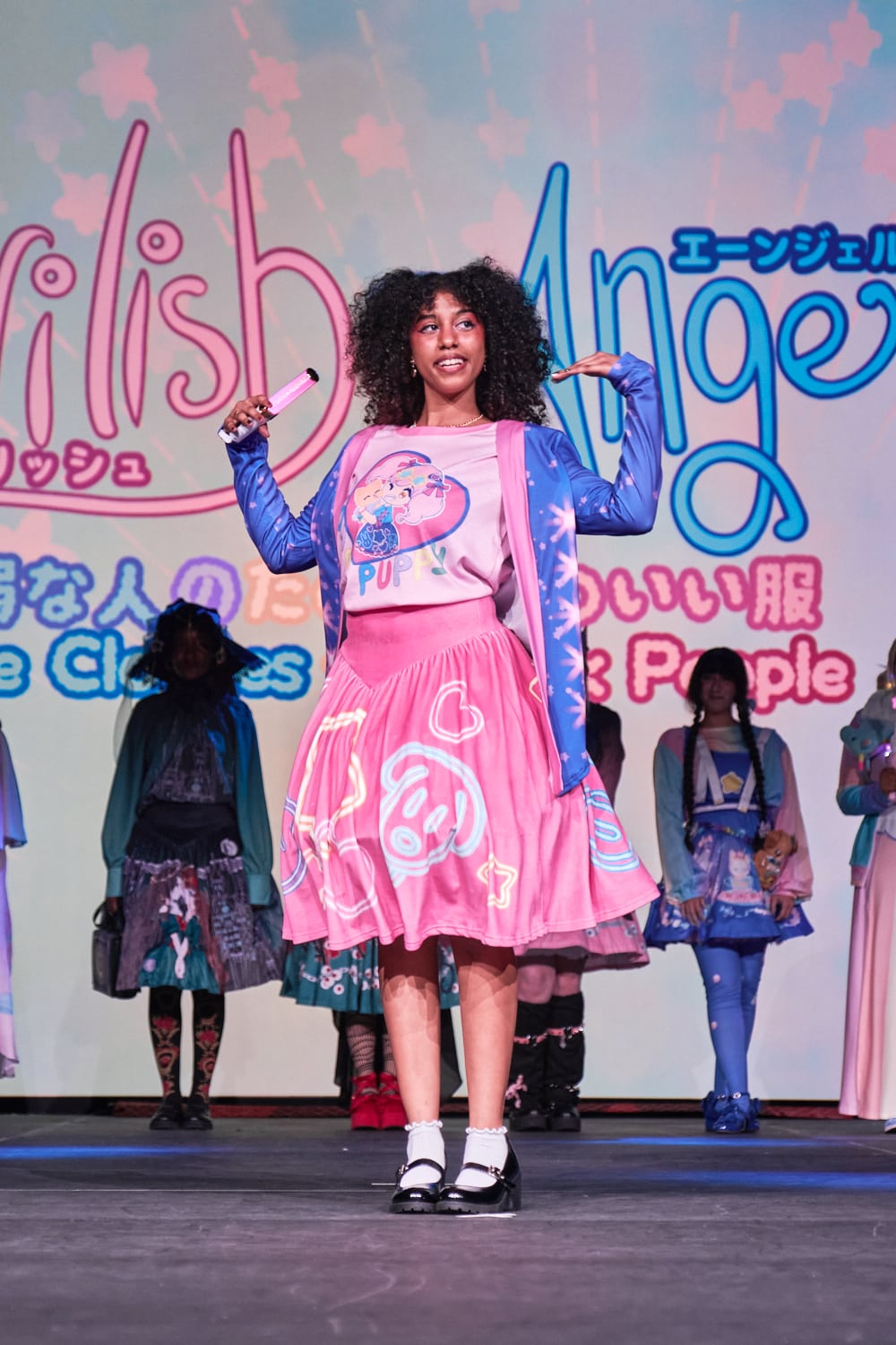 Cute model wearing blue and pink cardigan with pink heart T-shirt and pink circle skirt with neon light motifs - full body pose 1.