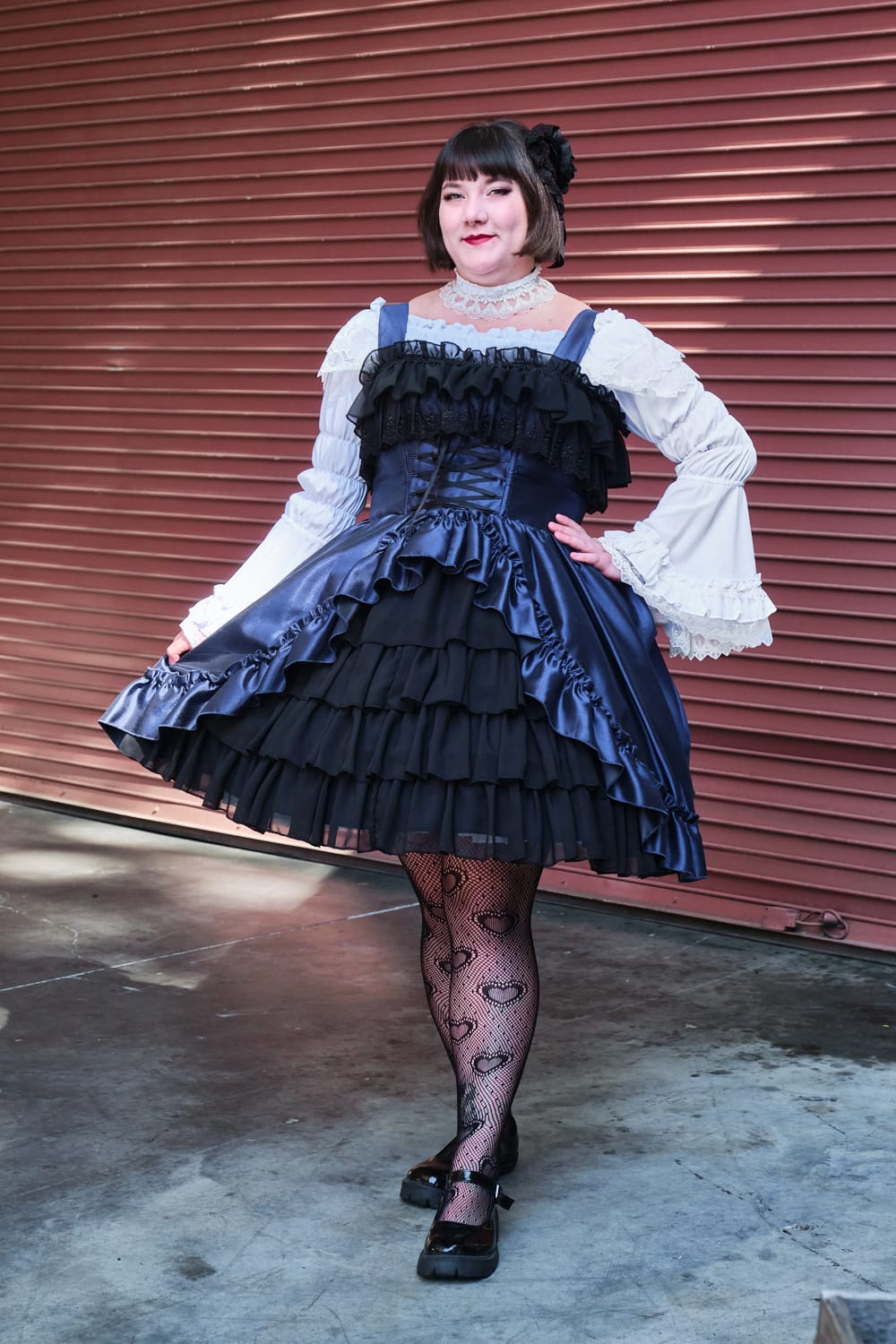 Atelier Pierrot plus size gothic lolita model wearing navy and black bustle corset jumperskirt with white princess sleeve blouse - full body standing pose 6.