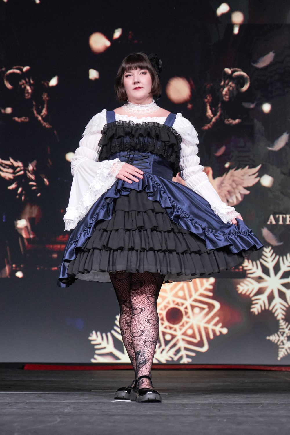 Atelier Pierrot plus size gothic lolita model wearing navy and black bustle corset jumperskirt with white princess sleeve blouse - full body standing pose 1.