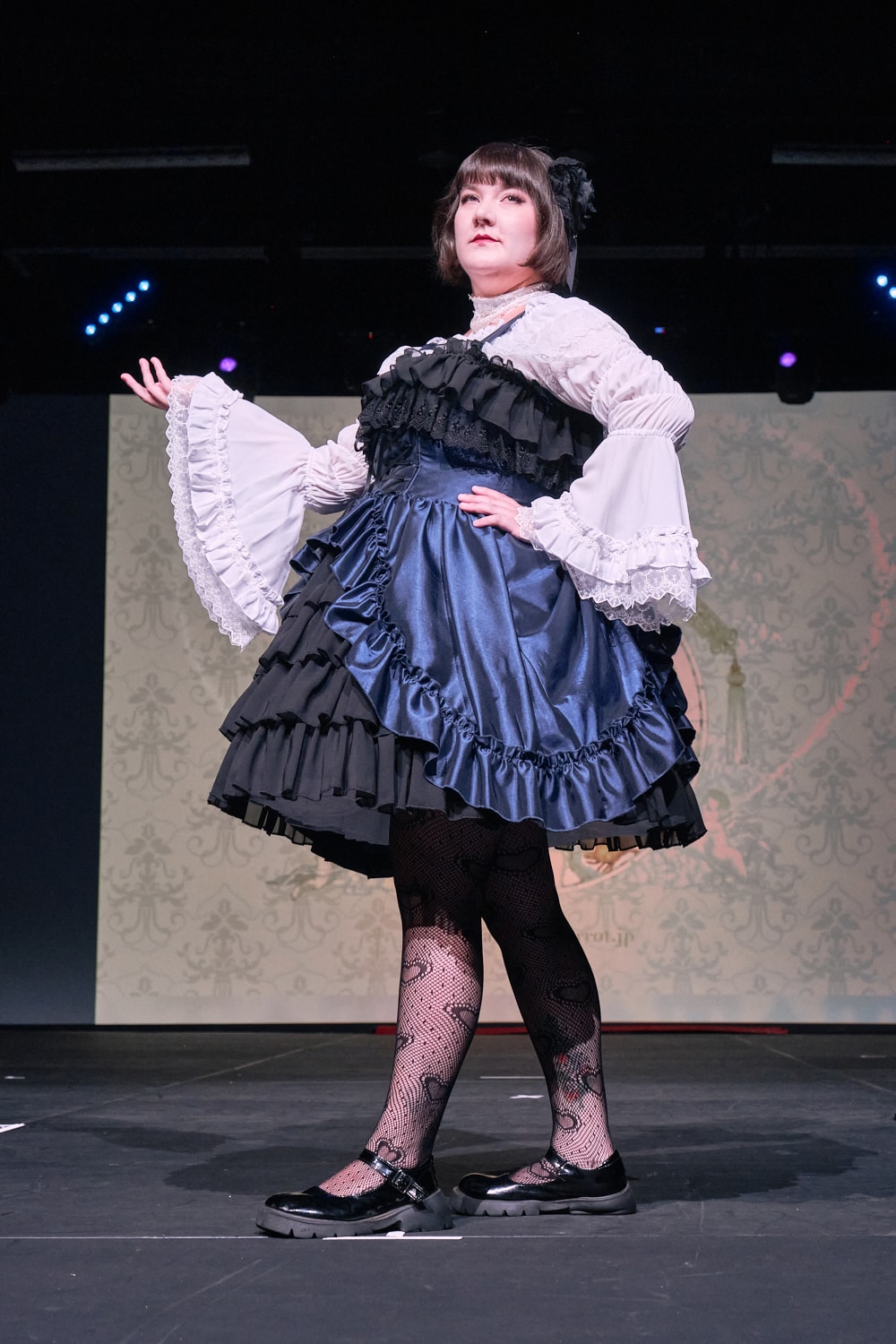 Atelier Pierrot plus size gothic lolita model wearing navy and black bustle corset jumperskirt with white princess sleeve blouse - full body standing pose 4.
