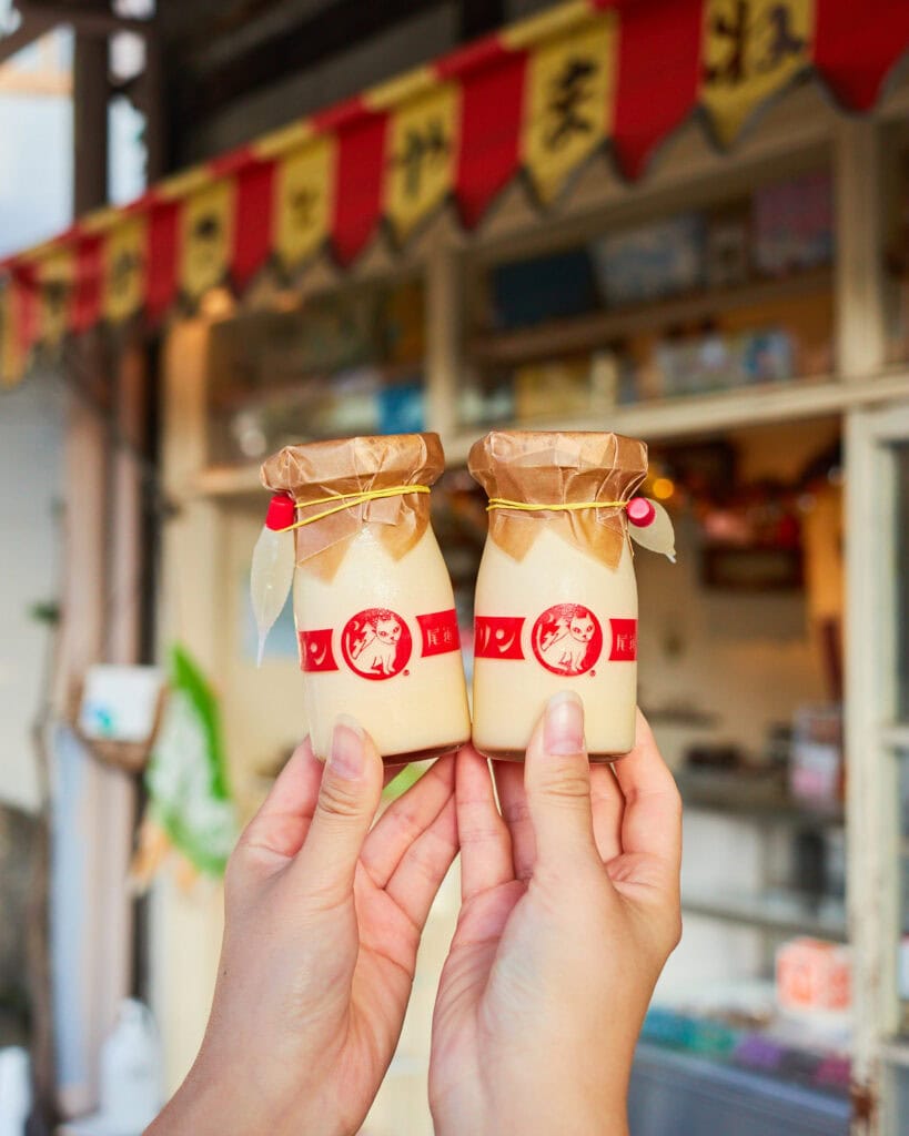 Hassaku orange pudding in small milk jars being held next to each other in front of the store front