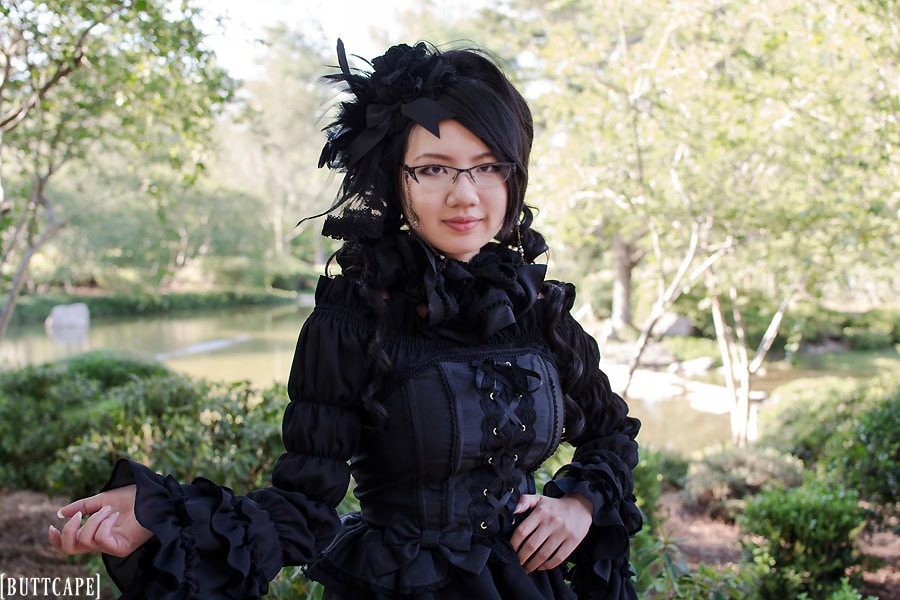 All black wearing gothic girl standing in park with frilly details.