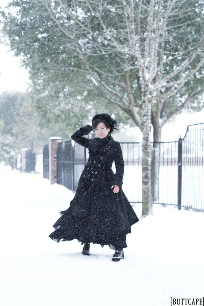 Smiling Victorian gothic person standing in snow.