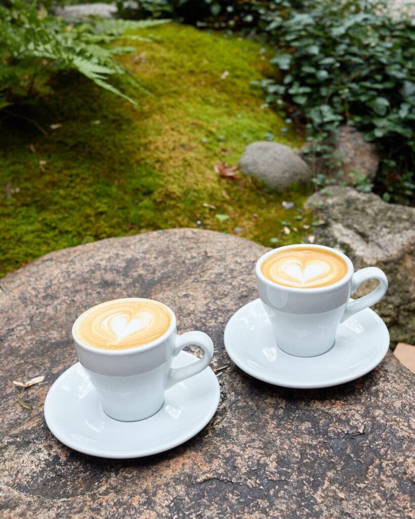 Two Weekenders Coffee Roasters cappuccinos in white cups on a rock in Japanese garden