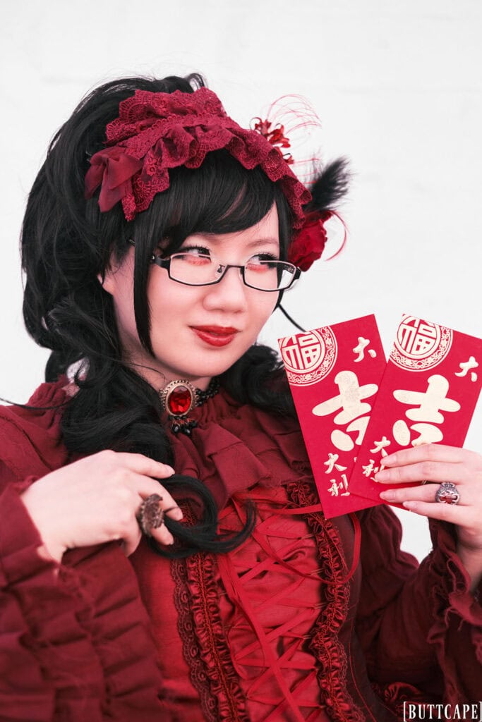 Portrait of all red lolita outfit. Subject is holding a pair of red paper envelopes for Lunar New Year.