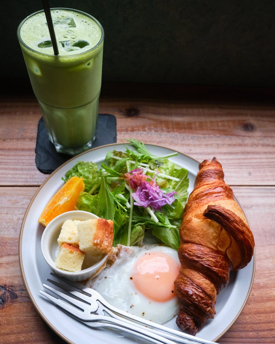 choueccha breakfast plate with croissant, fried egg, salad, orange slice, and pound cake