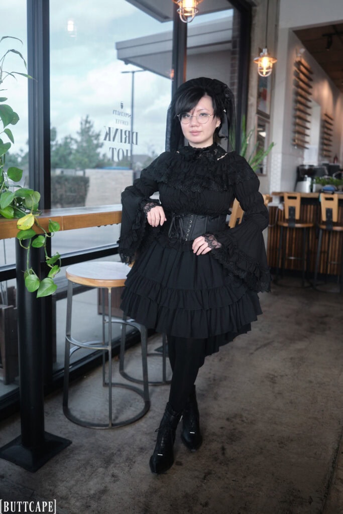Stephano wearing all black gothic lolita outfit with veil, dramatic princess sleeves, ruffle skirt, black tights, and mid calf boots.