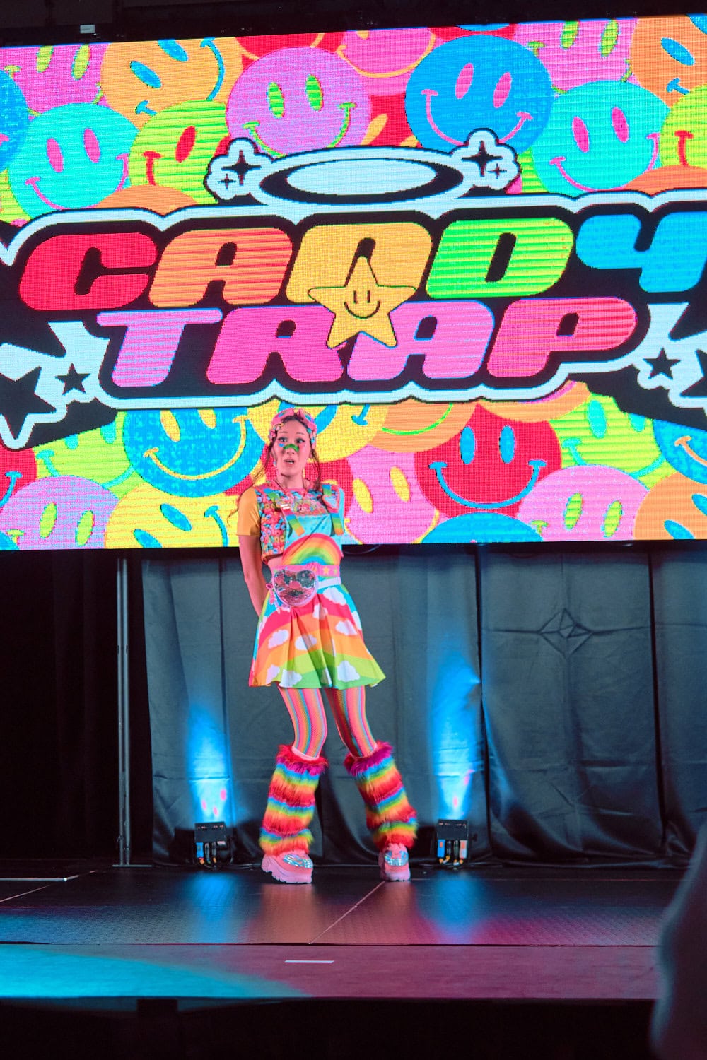 Candy Trap model #4 wears rainbow print t-shirt and matching A-line skirt with vertical rainbow stripe tights and fuzzy leg warmers.