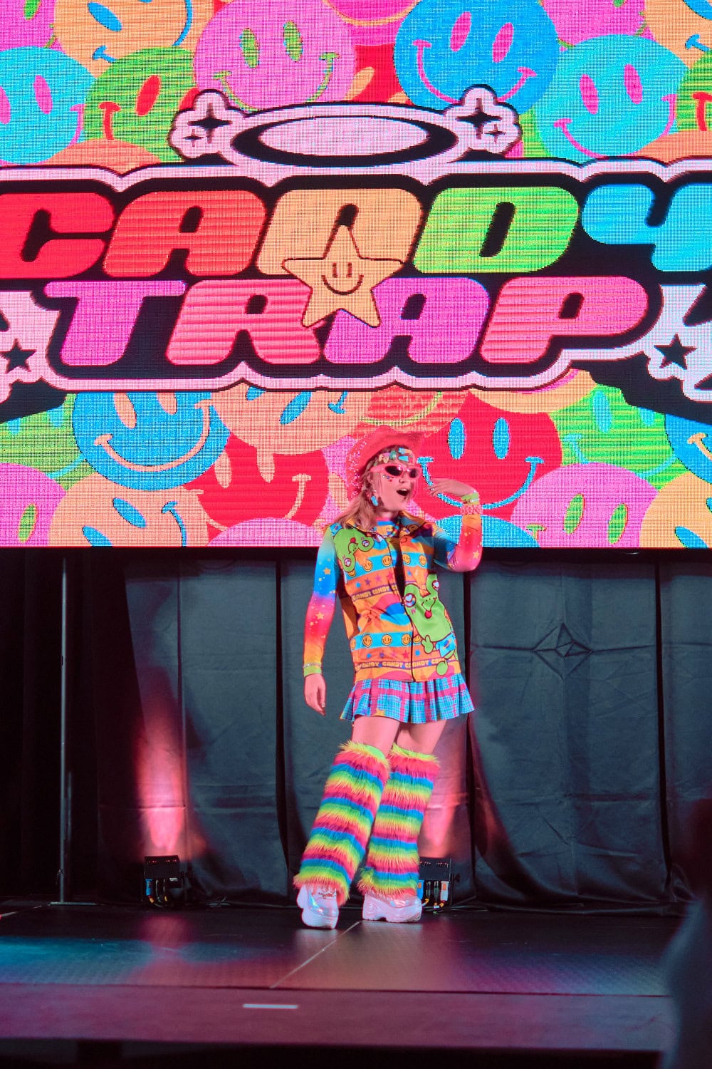 Candy Trap model #6 wears funky sunglasses, printed frog parka, plaid skirt, and fuzzy leg warmers.