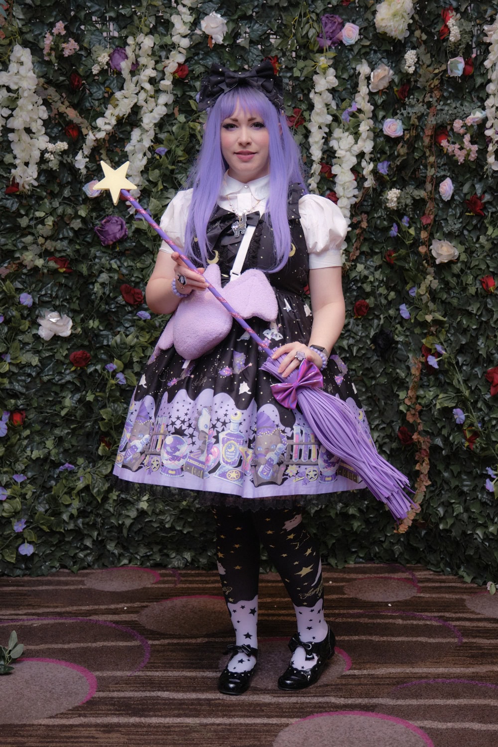 Witch theme sweet lolita standing in front of floral wall.