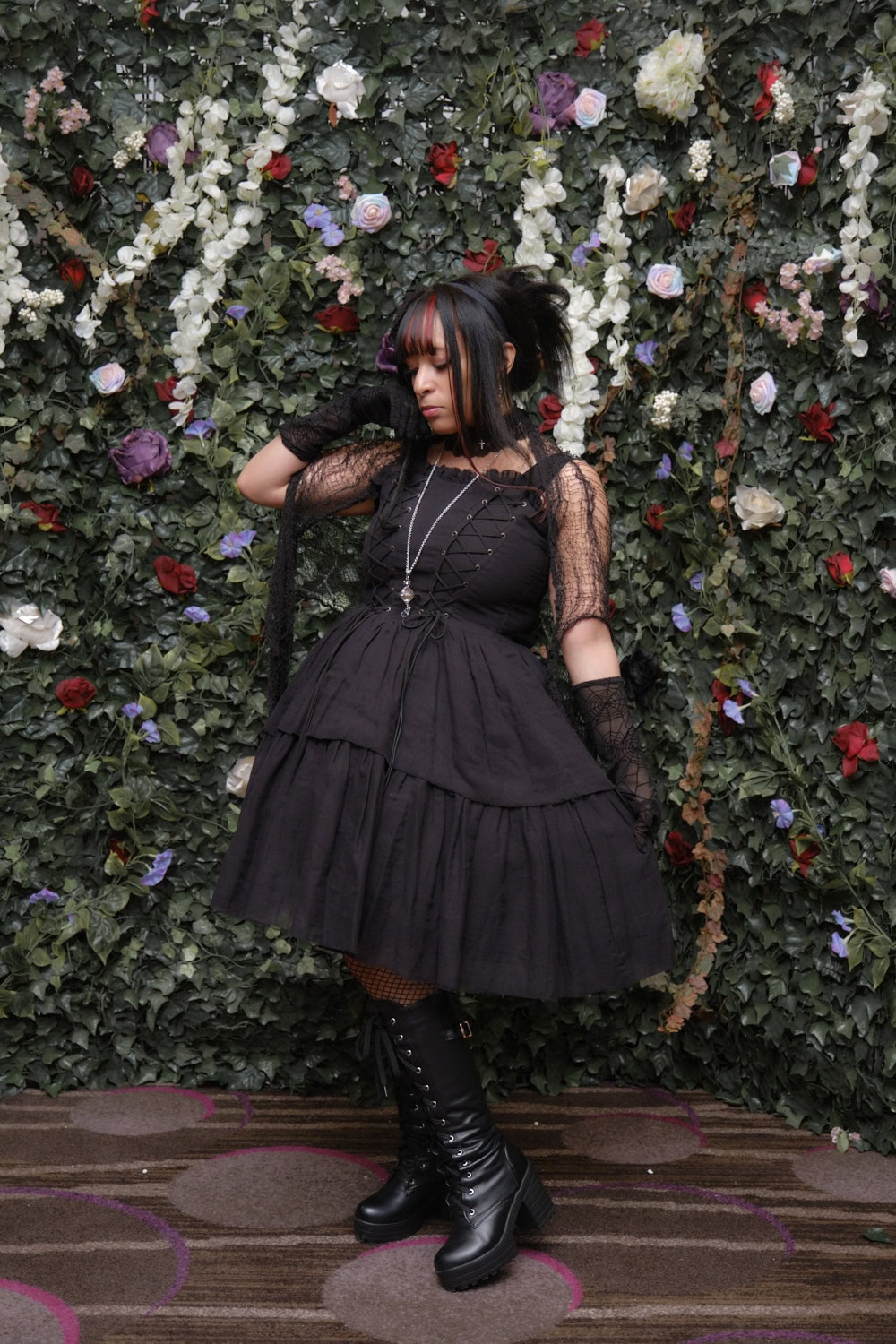 Gothic lolita standing in front of floral wall.