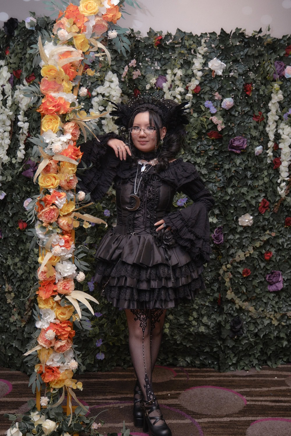 Gothic lolita standing in front of floral wall.