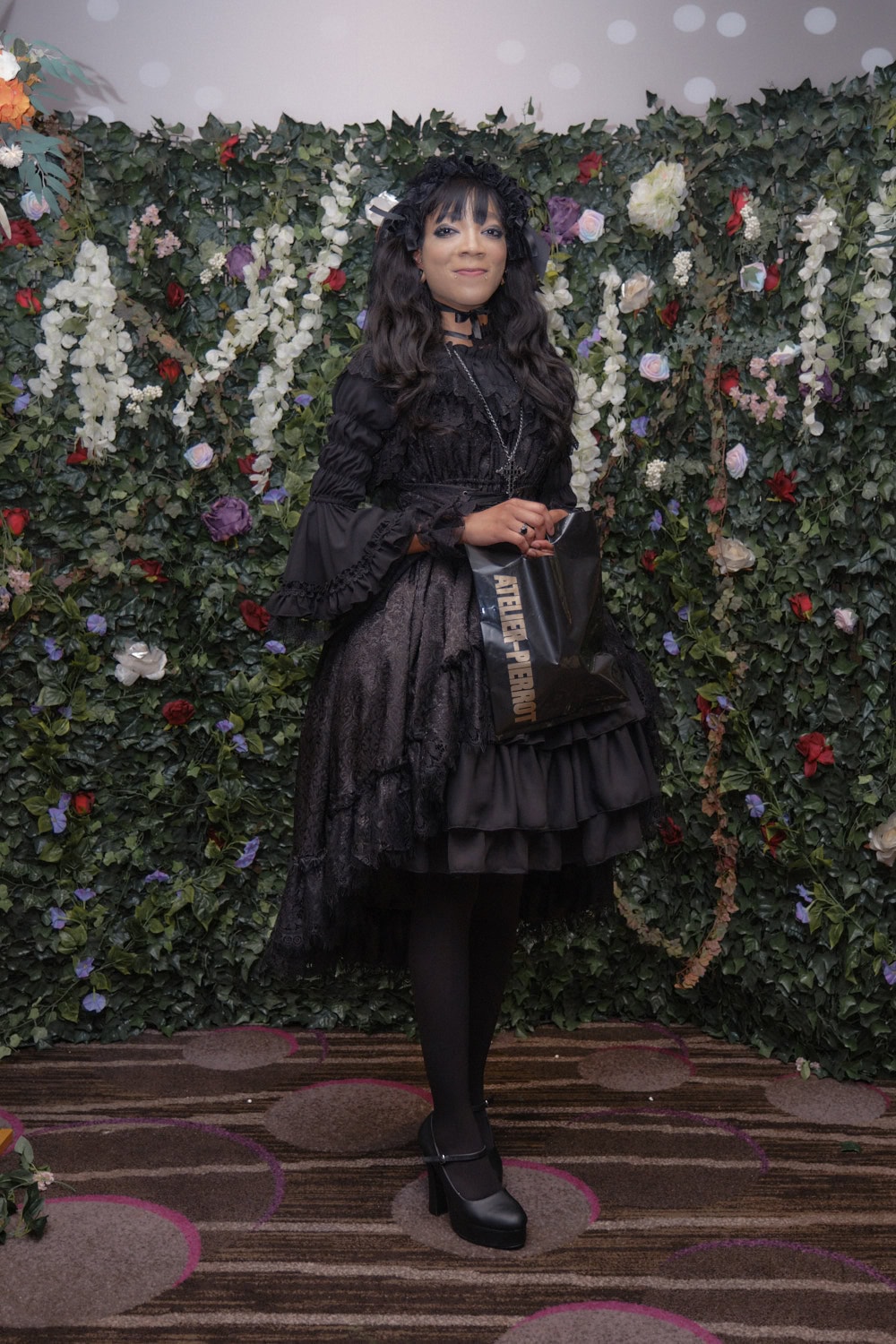Gothic lolitas standing in front of floral wall.