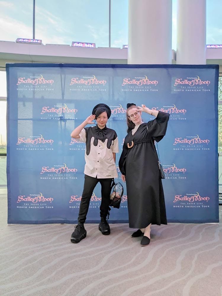 Two people posing in front of Pretty Guardian Sailor Moon The Super Live backdrop