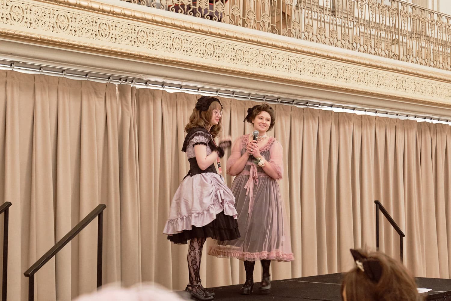 Two event hosts standing on stage talking with microphones.