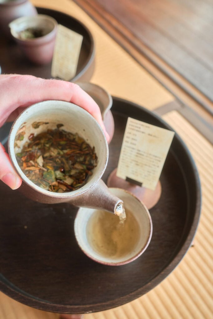 Tea from tea stand yamate being poured from a hand made ceramic tea pot into a tea cup