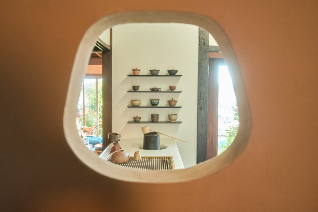 Photo of Tea Stand Yamate's tea pot collection mounted on a wall with a caster iron water heater next to a sink.