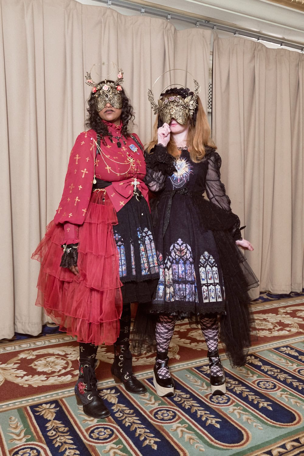 Two gothic lolitas wearing matching dresses and ornate masks.