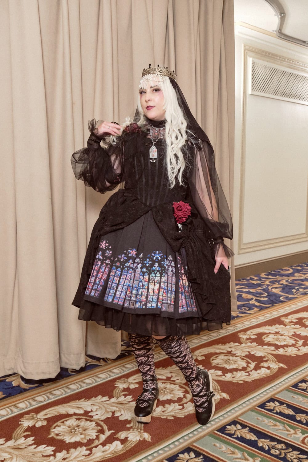 Gothic lolita wearing crown, veil, and stained glass print dress with corset.